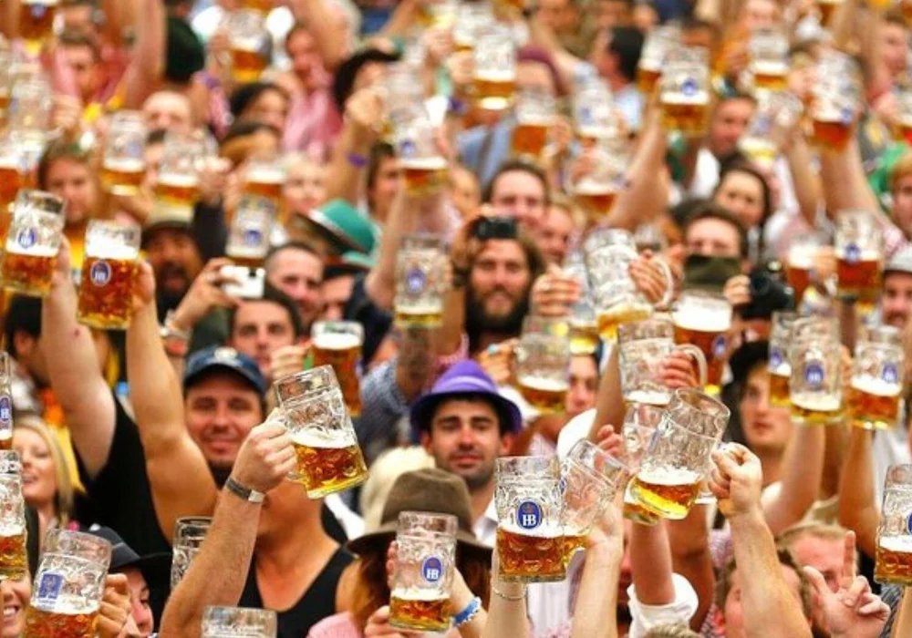 Oktoberfest festivalgoers raising large glass beer mugs in a crowded, lively beer tent