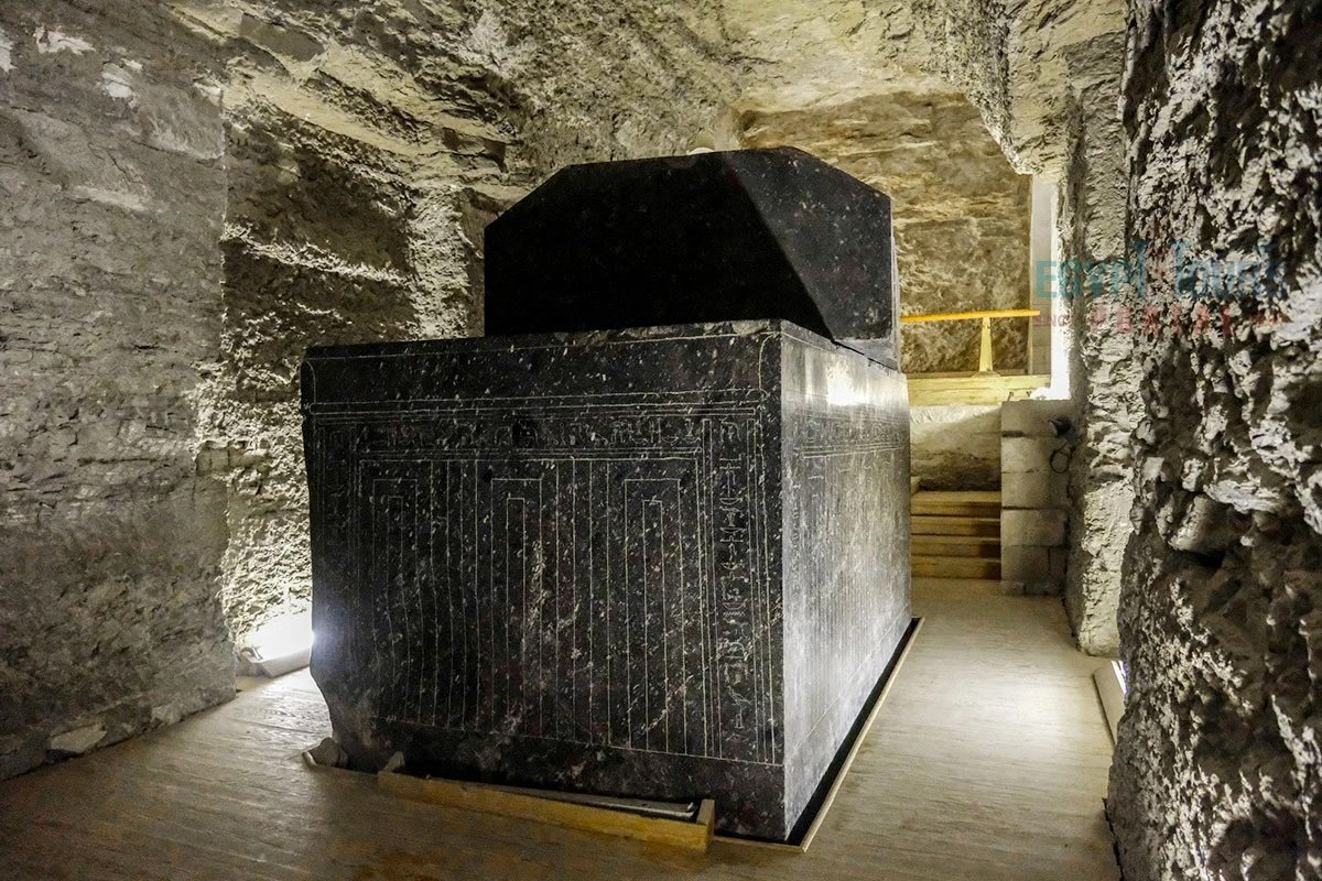 A large inscribed stone sarcophagus with a heavy raised lid stands inside an underground gallery at Saqqara.